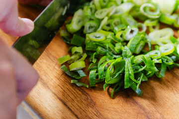 slicing fresh green onions with chef's knife, in a wooden board