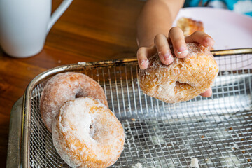kids hand pick up freshly fried donuts with sugar powder on a cooling rack