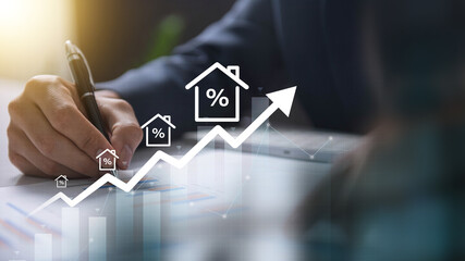 Real Estate Market Growth with Rising Interest Rates concept. Close-up of a person writing on a tablet with an upward graph and house icons, representing real estate growth and interest rates.