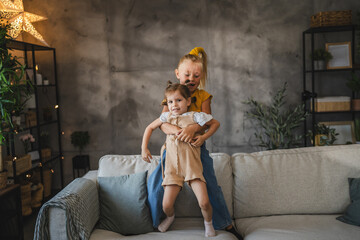 Two young girls play together on the sofa at home