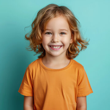 Portrait of a sandy-haired child smiling warmly with joy against a vibrant blue background in casual orange attire.