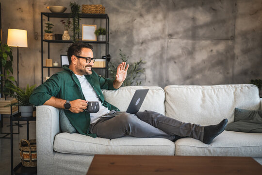 Adult man sit on sofa greeting and have video call on laptop at home
