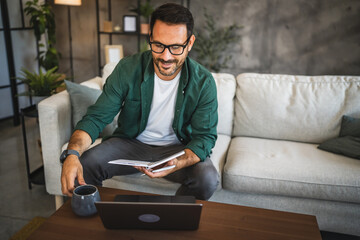 Adult man work from home with laptop and documents on the sofa