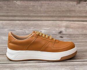 Casual style sneaker, light brown and white on a wooden background, left side
