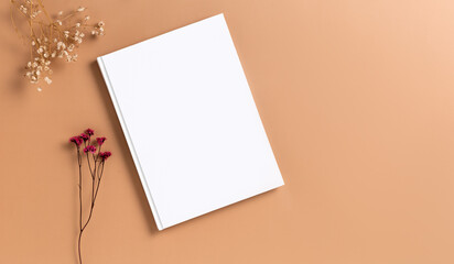 Mockup of a white hardcover book on a brown dark beige background dried gypsophila flower. Blank template for your design and advertising in a minimalist style flat lay