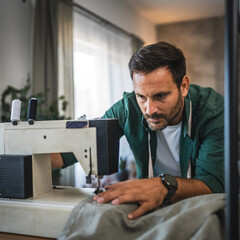 Adult man tailor, designer work at sewing machine in cozy home setting