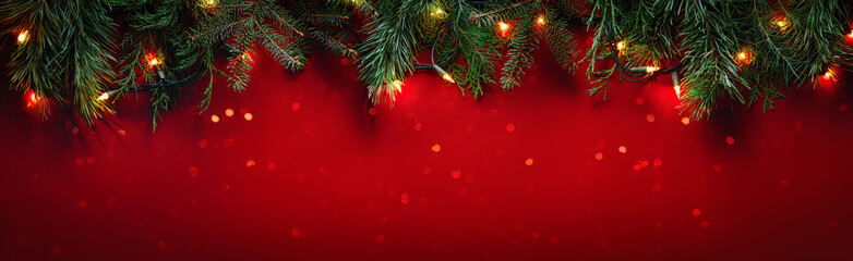 Christmas fir branches on glittering red background with winter holiday lights