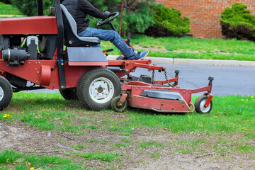 An employee of municipality mows grass with lawn mower tractor at landscaping work