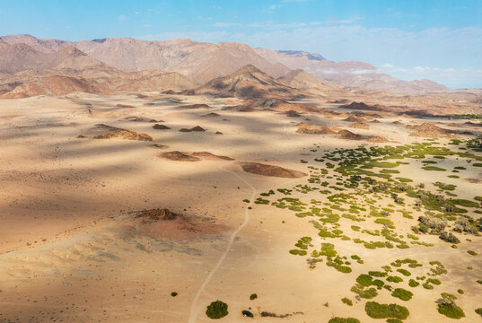 Aerial view of The dry bed of the Ugab river cuts through arid desert plains, behing the Brandberg, Namibia's highest mountain, aerial view, drone shot, Damaraland, Namibia.