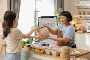 Woman receiving food delivery from restaurant worker in a cozy kitchen setting, promoting small business and home-based services.