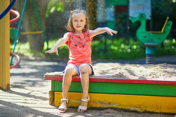 Adorable preschooler girl having fun on playground in sandpit