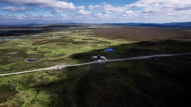 Aerial Orbit Shot, Explore the barren Moorland landscape of Flatruet as a car and camper pass a lone red building, highest country road in J&auml;mtland, H&auml;rjedalen Sweden