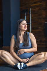 Pregnant woman in the gym doing warm-up. Sitting on a yoga mat.