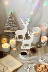 Various Christmas decorations, lit candles, cup of tea or coffee, cookies, books, presents and soft blanket on the table. Holiday hygge at home. Selective focus.