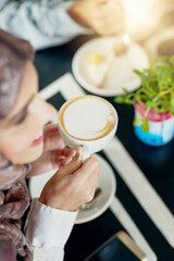 Happy woman, coffee and drink with foam at cafe for beverage, morning or breakfast at indoor restaurant. Female person, caffeine or cappuccino in hijab with smile, cup or mug for mocha or latte