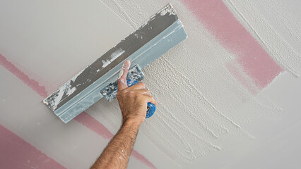 The worker make a plasterboard ceiling. He does sealing of joints with gypsum putty on plaster...
