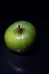 Green juicy apple with water drops on dark background. Still life.