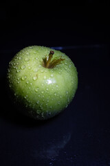 Green juicy apple with water drops on dark background. Still life.