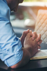 Obraz premium Pray and bible concept. Hand in hand together on bible by Caucasian man (worship christian), thinking and closed her eyes at church. Person side view, male praying, hope for peace-vertical image.