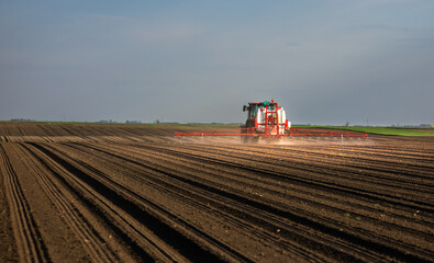 Fototapeta premium Tractor spraying land in sunset.
