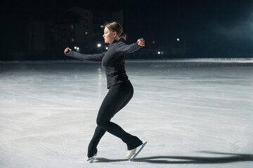 Beautiful young woman ice skating and performing short program over city outdoor ice arena. Winter activities concept © olinchuk