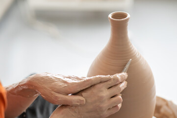 A potter works with a tool on a potter's wheel leveling the surface of a vase. Close-up of a man's...
