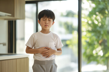 Young boy is feeling unwell and holding his stomach, experiencing discomfort or pain in his abdomen
