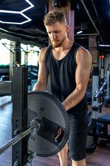 An athlete in the gym swings triceps with a barbell. Sports lifestyle.