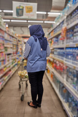Asian woman wearing hijab shopping at supermarket looking for daily needs between store shelves