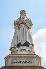 Fototapeta premium The monument dedicated to Leonardo da Vinci stands proudly in Piazza della Scala, Milan, showcasing intricate sculptural details against a clear blue sky, celebrating the artist's legacy.
