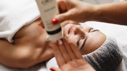 Close-up of a cosmetologist dispensing cream and massaging a young client’s face. This highlights the professional care and technique used in high-quality skincare treatments.