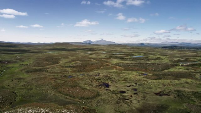 Drone ascending above the expansive, high fell and barren moorland with waterholes and winding streams of Flatruet in Sweden, showcasing its stunning natural beauty and unique terrain under a blue sky