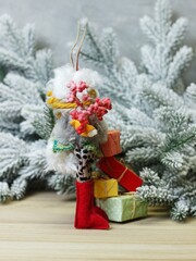 Christmas character rabbit with colorful ears in a sweater with presents in his hands on the background of pine branches