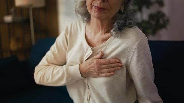 Senior woman feeling acute chest pain while sitting on couch, heart failure