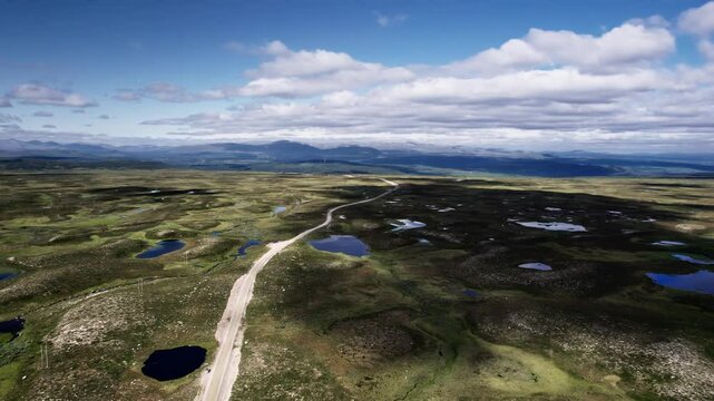 Flying backwards over the winding country road on Flatruet high Fell in J&auml;mtland, H&auml;rjedalen Sweden, showcased by lush moorland and the mountains of V&aring;l&aring;dalen Nature Reserve in the background