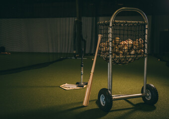 Baseball Bat Leaning on Ball Cart Filled with Baseballs