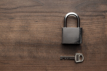 Closed padlock and one key on the brown wooden table background with copy space.