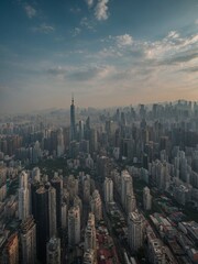 Obraz premium Panoramic view of crowded skyline of major metropolitan city, likely Hong Kong or Shanghai, with numerous high-rise buildings and skyscrapers stretching out as far as eye can see under cloudy, hazy
