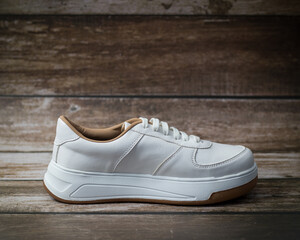 Elegant white eco-leather sneakers with brown sole detail, left., on a wooden background