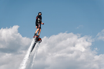 Athlete is flying using flyboard powerful water jet pack on the background of cloudy sky