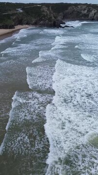 Stunning 4K drone footage flying over the Atlantic Ocean at Odeceixe Beach on Portugal&rsquo;s Vicentine Coast, with breathtaking views of the cliffs and the iconic rock formation in the background
