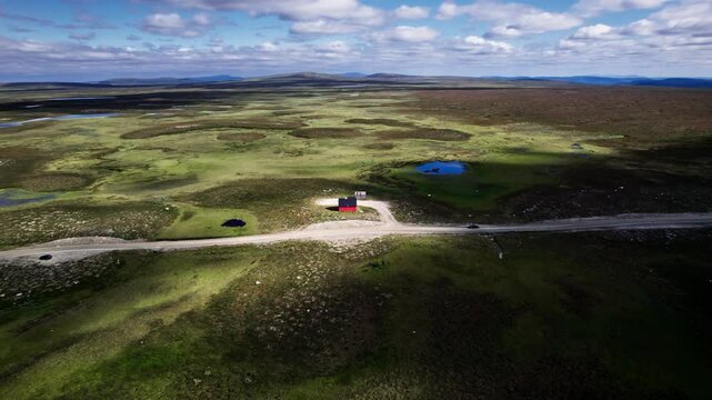 Aerial Orbit Shot: car traveling along highest country road Flatruetv&auml;gen in Sweden, passing an red building against the vast open landscape of Flatruet high fell plateau and mountains