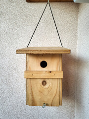 wooden bird house hung on a house wall, entrance hole for small European birds
