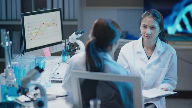 Female scientists talking discussed on graph on computer for result of the experiment report in laboratory for research on pharmacy medical for healing and antibody for protect disease and virus