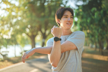 Happy sporty asian young male in sportswear stretching his arms or warming up his body before...