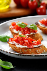 Cherry tomatoes and cream cheese bruschettas with fresh basil leaves.