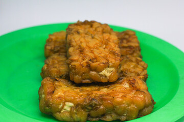 Fried tempeh food is served on a small green plate with a white background