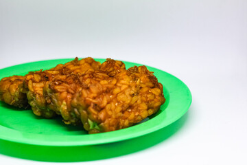 Fried tempeh food is served on a small green plate with a white background
