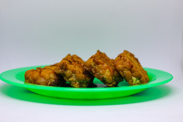 Fried tempeh food is served on a small green plate with a white background