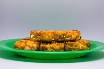 Fried tempeh food is served on a small green plate with a white background